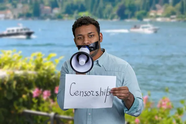 黒いテープを口にし 海のぼやけた背景に立っている若い男 検閲の概念 — ストック写真