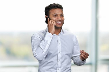 Beyaz gömlekli neşeli genç iş adamı cep telefonuyla konuşuyor. Görüntü arkaplanı.