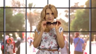 İçeride güneş gözlüğü takan sarışın bir kadının portresi. Arka planda sokaktaki insan kalabalığı.