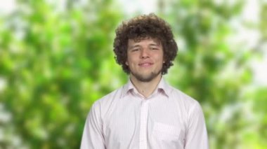 Açık havada rüya gören kıvırcık saçlı mutlu genç adam. Arkaplanda ağaç yaprakları.
