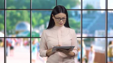 Esmer, Asyalı bir iş kadınının tablet bilgisayar kullanarak kaydırma ve kaydırma kullandığı portresi. Arka plandaki kapalı pencere.