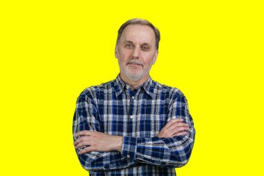 Kolları bağlı, kendinden emin, yakışıklı bir ihtiyarın portresi. Pastel sarı arka planda izole edilmiş.