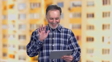 Son sınıf öğrencisinin tabletini kullanırken çekilmiş bir portresi. Yaşlı bir adam dışarıda elini sallıyor. Arka plandaki konut binası..