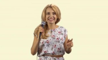 Mikrofonda şarkı söyleyen mutlu sarışın bir kadının portresi. Açık sarıda izole edilmiş..