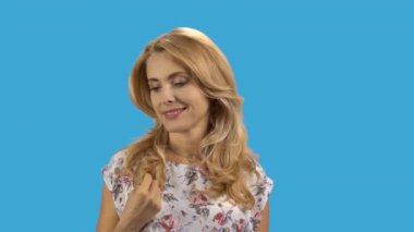 Sarı saçlarını kıvıran olgun, beyaz bir kadın. Mavi üzerine izole edilmiş..