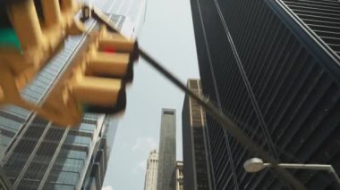 Manhattan, New York 'ta arka planda yüksek gökdelenleri olan bir trafik ışığı manzarası. Görüntü şehir mimarisini ve hareketli sokak ortamını vurguluyor.