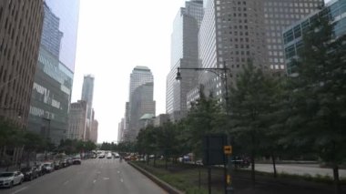 New York Citys Finans Bölgesi 'ndeki modern gökdelenlerin manzarası, ağaçlarla çevrili caddeler tarafından çerçevelenmiş. Kentsel mimari ve yeşil alanların karışımı şehirlerin dinamik karakterini vurgular.