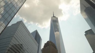Manhattan şehir merkezindeki diğer modern gökdelenlerle çevrili bir Dünya Ticaret Merkezi manzarası. Dramatik gökyüzü ve cam binalardaki yansımalar büyüleyici bir şehir manzarası yaratıyor..