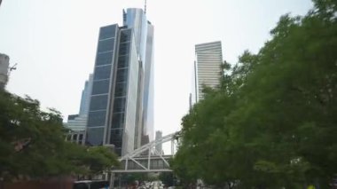 New York City, New York, ABD - 08.01.2024: Manhattan şehir merkezindeki düz gökdelenler ve binaları birbirine bağlayan yaya köprüsü. Ön plandaki ağaçlar yeşillik katıyor