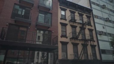 New York City, New York, ABD - 08.01.2024: Modern kırmızı tuğlalı bir apartman ve klasik yangın merdivenleri olan tarihi bir bej bina. Mimari tarzların karışımı