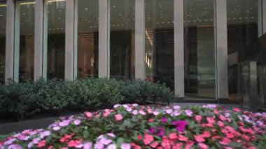 Geniş cam cepheli modern bir ofis binasında ön planda canlı bir çiçek yatağı yer alır. Camdaki yansımalar çağdaş mimariye derinlik katıyor..