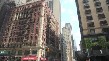 New York City, New York, ABD - 08.01.2024: Meşgul bir şehir manzarasında yangın merdivenleriyle süslenmiş canlı bir kırmızı tuğla bina göze çarpıyor. Modern gökdelenler ve mağazalar klasik ile bir karşıtlık yaratır