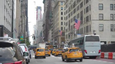 New York City, New York, ABD - 08.01.2024: Midtown 'da kalabalık bir New York caddesi, sarı taksiler, otobüsler ve arabalarla dolu. İkonik Amerikan bayrakları binaları süslüyor, şehirleri gösteriyor.