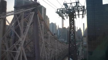 Roosevelt Adası Tramvay Kulesi 'nin yanındaki Queensboro Köprüsü' nün detaylı yapısı. Manhattan silueti, huzurlu bir günbatımında arka planda yükselir..