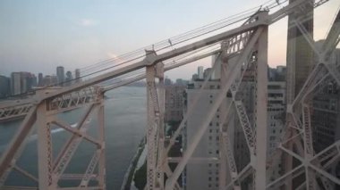 Queensbou Queensboro Köprüsü 'nün karmaşık çelik yapısı Doğu Nehri' nin üzerinde duruyor. Modern şehir binaları ve sakin nehir suları bu ikonik New York şehri manzarasını çerçeveliyor.