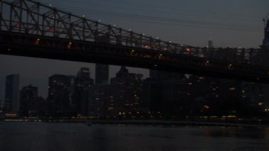 Queensboro Köprüsü, gece yumuşak ışıklarla parlayarak Doğu Nehri 'nin üzerine uzanır. Manhattan ufuk çizgisi ve nehir köprüleri aydınlatarak huzurlu bir şehir manzarası yaratıyor..