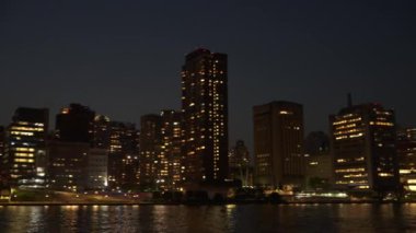 İkonik Queensboro Köprüsü ve canlı şehir silueti gece gökyüzüne karşı güzel bir şekilde parlıyor. Nehirdeki parıldayan yansımalar sakin ve büyüleyici bir şehir manzarası yaratır..