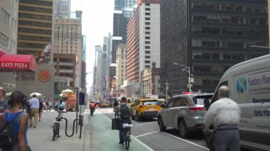 New York, New York, ABD - 07.29.2024: Yayalar ve bisikletçiler araçlar ve yüksek binalarla dolu kalabalık bir şehir caddesinde geziniyorlar. Büyük bir şehrin atmosferi ve insanlar koşuşturuyor.