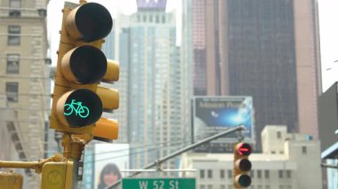New York 'ta yoğun bir kavşakta yeşil bir bisiklet sinyali yanıyor. Bisikletçiler şehir manzarasında gezinirken gökdelenler arka planda.