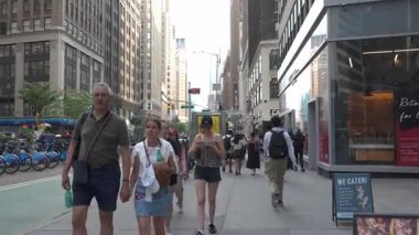 New York City, New York, ABD - 07.29.2024: İnsanlar kalabalık bir Manhattan caddesi boyunca uzun binalar ve dükkanlarla çevrili bir şekilde yürürler. Atmosfer yayalarla dolu. Yaz güneşinin tadını çıkarıyorlar.