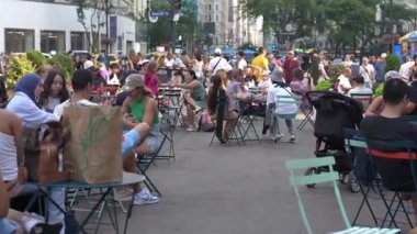 New York City, New York, ABD - 07.29.2024: İnsanlar kalabalık bir Manhattan meydanında açık hava masalarında rahatlar, kahkaha ve sohbetle dolu canlı atmosferin tadını çıkarırlar. Çeşitli aktiviteler