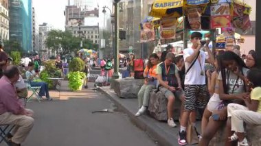 New York City, New York, ABD - 07.29.2024: Manhattan 'da insanlar bir sokak köşesinde toplanırken hayat dolu bir gün yaşanıyor. Bazıları banklarda dinlenirken, diğerleri yakındaki bir yiyecek tezgahını ziyaret ediyor. Atmosfer...