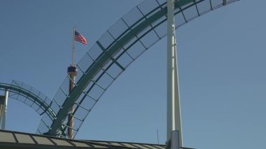 Hız treni, parlak mavi bir gökyüzünün altında dikey bir döngü içinde hız yapar. Arka planda bir Amerikan bayrağı dalgalanıyor ve heyecan verici sahneye vatansever bir dokunuş ekleniyor..