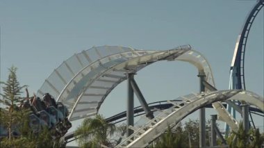 Ziyaretçiler, açık mavi bir gökyüzünün altında virajları ve dönüşleri dönerken lunaparktaki gezintilerin heyecanını yaşıyorlar. Enerjik atmosfer eğlence için mükemmel bir gün yaratıyor..