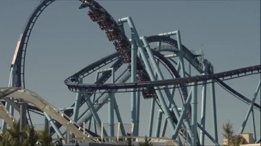 Ziyaretçiler, güneşli bir öğleden sonra eğlence parkında kıvrımlar ve dönüşlerle dolu yüksek enerjili bir hız trenine biniyorlar..