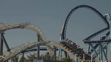 Orlando, Florida, ABD - 11.15.2024: Döngü ve düşüşler arasında hızla süzülen hız treninin heyecanının tadını çıkarın. Heyecan arayanlar, bu canlı sahil şeridinde açık mavi gökyüzünün altında koşuşturmayı deneyimlerler..