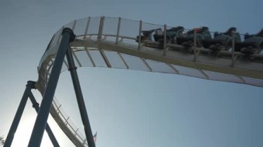 Heyecan arayanlar, deniz eğlence parkında keyifli bir lunapark treninin tadını çıkarıyorlar. Bardak altlığı yükseldikçe ve mavi gökyüzünün altına daldıkça heyecan artar..