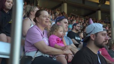Orlando, Florida, ABD - 11.15.2024: Bir anne diğer izleyicilerle bir performans izlerken genç kızını kucağına alır. Küçük kız meraklı ve sakin görünüyor. Kalabalık ortamda hassas bir an yaratıyor..