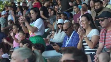 Orlando, Florida, ABD - 11.15.2024: Canlı bir kalabalık açık hava stadyumunda bir gösteri izliyor. İnsanlar gülümsüyor, sohbet ediyor ve telefonlarıyla anı kaydediyor. Neşeli ve rahat bir atmosfer yakalıyorlar..