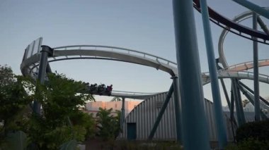 Akşam saatlerinde lunaparktaki lunaparktaki hız trenlerinin heyecanını yaşayın. Konuklar çığlık atıyor ve tropikal manzaranın ortasındaki heyecan verici virajların tadını çıkarıyorlar..