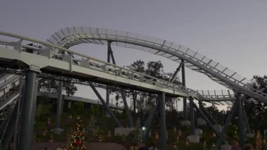 Orlando, Florida, ABD - 11.15.2024: Deniz Dünyası macera parkında gece çökerken heyecan verici lunapark trenine konuklar katılıyor. Renkli ışıklar yemyeşil ortamda şenlikli bir atmosfer yaratır..