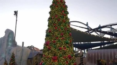 Orlando, Florida, ABD - 11.15.2024: Canlı tatil ışıkları uzun ağacı süslüyor, parkı bir kış harikalar diyarına dönüştürüyor. Misafirler, bu deniz manzarasının keyfini çıkarırken neşeli gösterilerin önünden geçiyorlar..