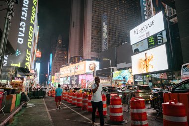 New York City, New York, ABD - 07.28.2024: İnsanlar New York Times Meydanı 'nda inşaat engellerini ve trafiği aşarak yürüyor. Dijital reklam panoları ve ışıklar sahneyi renk ve enerjiyle dolduruyor.