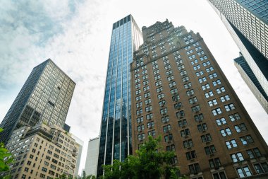 New York mimarisinin yukarıdan görünüşü modern kuleler ve geleneksel tuğla gökdelenlerin bir karışımını gösteriyor. Şehir silüeti yumuşak gün ışığında yükseliyor..
