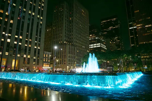 New York City, New York, ABD - 07.28.2024: Bir çeşmenin parlak ışıkları Manhattan 'ın hareketli sokaklarını gece aydınlatır. İnsanlar toplanıp, gökdelenlerle çevrili neşeli atmosferin tadını çıkarıyorlar..