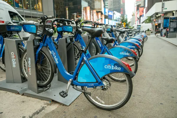 New York City, New York, ABD - 07.29.2024: Manhattan 'da bir bisiklet paylaşım istasyonuna park edilmiş bir dizi Citi bisikleti. Parlak şehir ışıkları ve arka planda yüksek binalar.