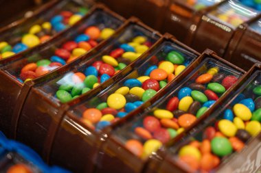 Bir dükkanda içi renkli çikolata şekerleriyle dolu kahverengi plastik şeker kutularının yakın çekimi. Parlak renkler kompartımanlarda göze çarpar.