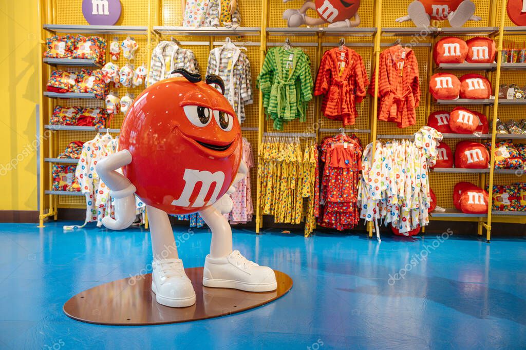 New York City, New York, USA - 07.29.2024: A red MMs statue stands proudly in front of shelves filled with themed clothing at the New York store.