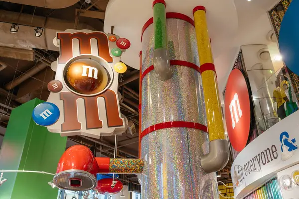 New York City, New York, ABD - 07.29.2024: MM 's şeker dükkanının iç çekimleri renkli tüpler, tabelalar ve neşeli şeker dekoru gösteriyor. Tavandan büyük bir MM amblemi askıya alındı.