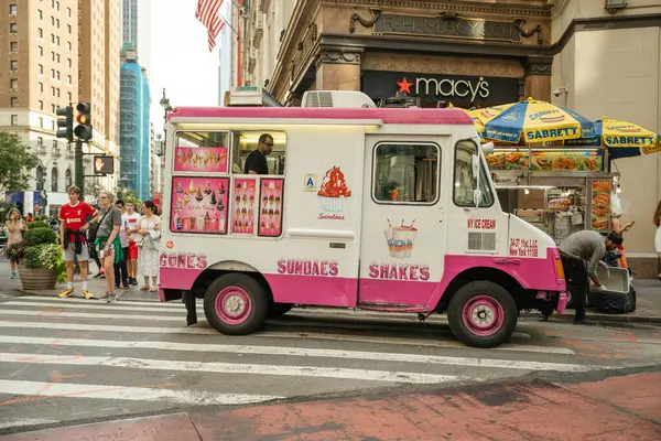 New York City, New York, ABD - 07.29.2024: Pembe ve beyaza boyanmış bir dondurma kamyonu New York 'ta Macys' in önünde dondurma, dondurma ve milkshake sunuyor. Yayalar ve yiyecek tedarikçileri sıcak ve canlı bir öğleden sonra kamyonun etrafını sardılar..