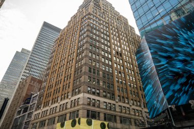 Tarihi kahverengi taşlı mimari ve yansıtıcı cam binaların bir karışımı bu Manhattan şehir merkezini tanımlar. Mavi soyut bir dijital ilan panosu sahneye kontrastlık ve canlılık ekler.