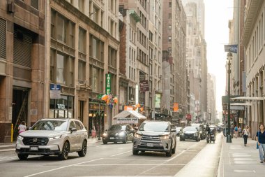 New York, New York, New York, ABD - 07.29.2024: Gün batımında Manhattan 'da kalabalık bir şehir merkezi boyunca birden fazla araba ve yayalar hareket ediyor. Yol uzun tarihi binalarla, mağazalarla ve barın önünde asılı bayraklarla dolu..