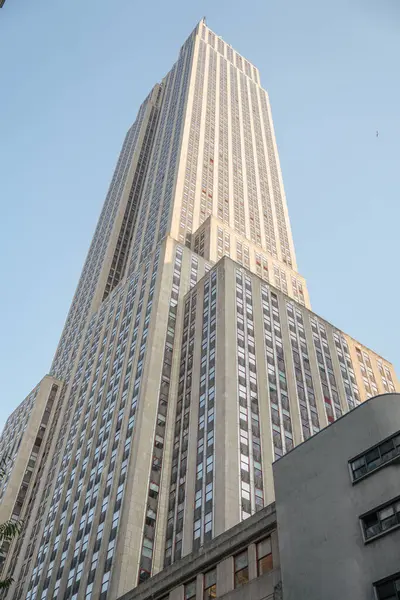 Caddenin yukarısındaki Empire State Binası. Yumuşak akşam ışığı banyosu. İkonik tasarımı ve yüksekliği açık mavi gökyüzüne karşı ufuk çizgisine hakim..
