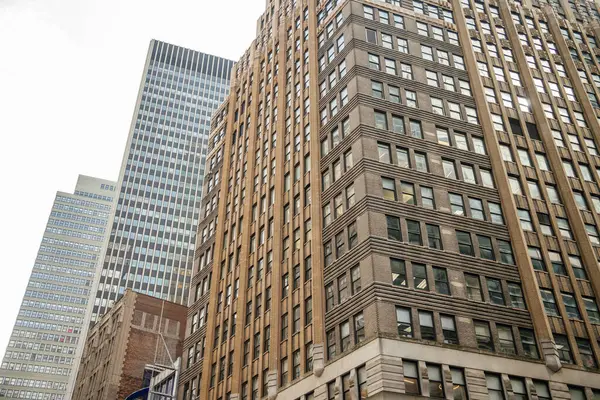 Manhattan şehir merkezindeki klasik ofis binaları ve gökdelenlerin detaylı bir görüntüsü. Fotoğraf, arkaplandaki pencereler, tuğla işleri ve zıt modern kuleleri vurguluyor.
