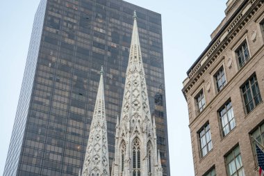 St. Patricks Katedrali 'nin zarif kuleleri modern bir gökdelenin cam cephesine çarpar. Bu ikonik karşıtlık New York 'un Manhattan şehrinin mimari çeşitliliğini yansıtır..