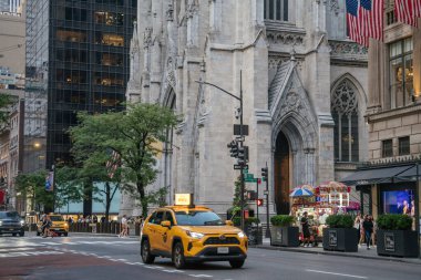 New York City, New York, ABD - 07.29.2024: Sarı bir NYC taksisi Beşinci Cadde 'deki St. Patricks Katedrali' nin büyük girişinden geçiyor. Gotik tarzı katedral modern gökdelenlerin ve hareketli şehir hayatının yanında gururla duruyor..